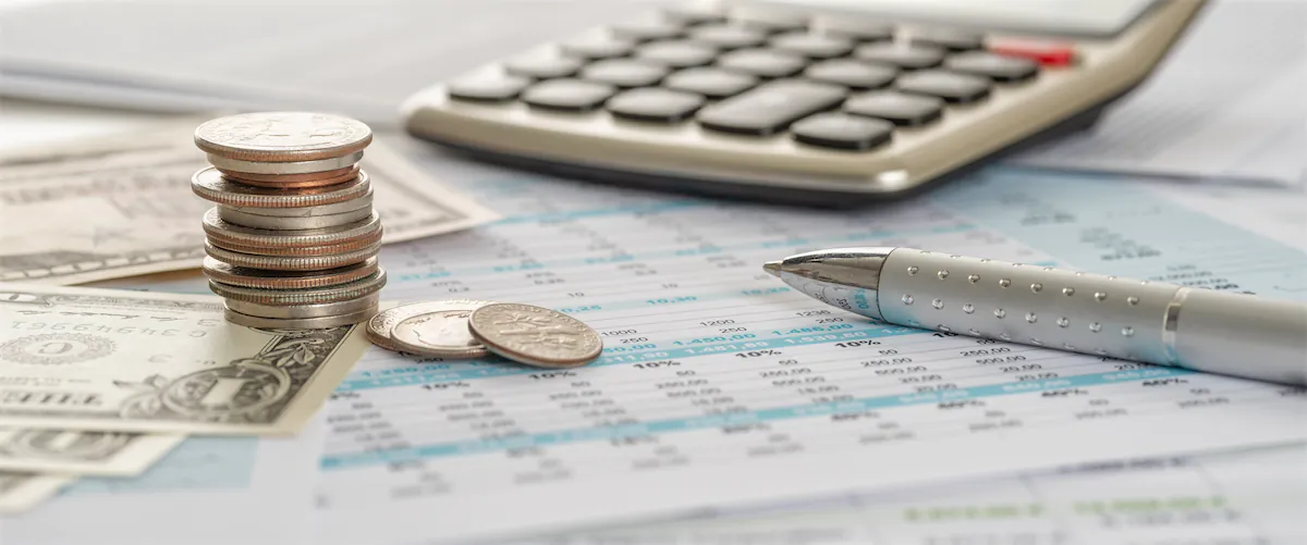 Stack of US coins, a pen, and a calculator, all on a paystub.