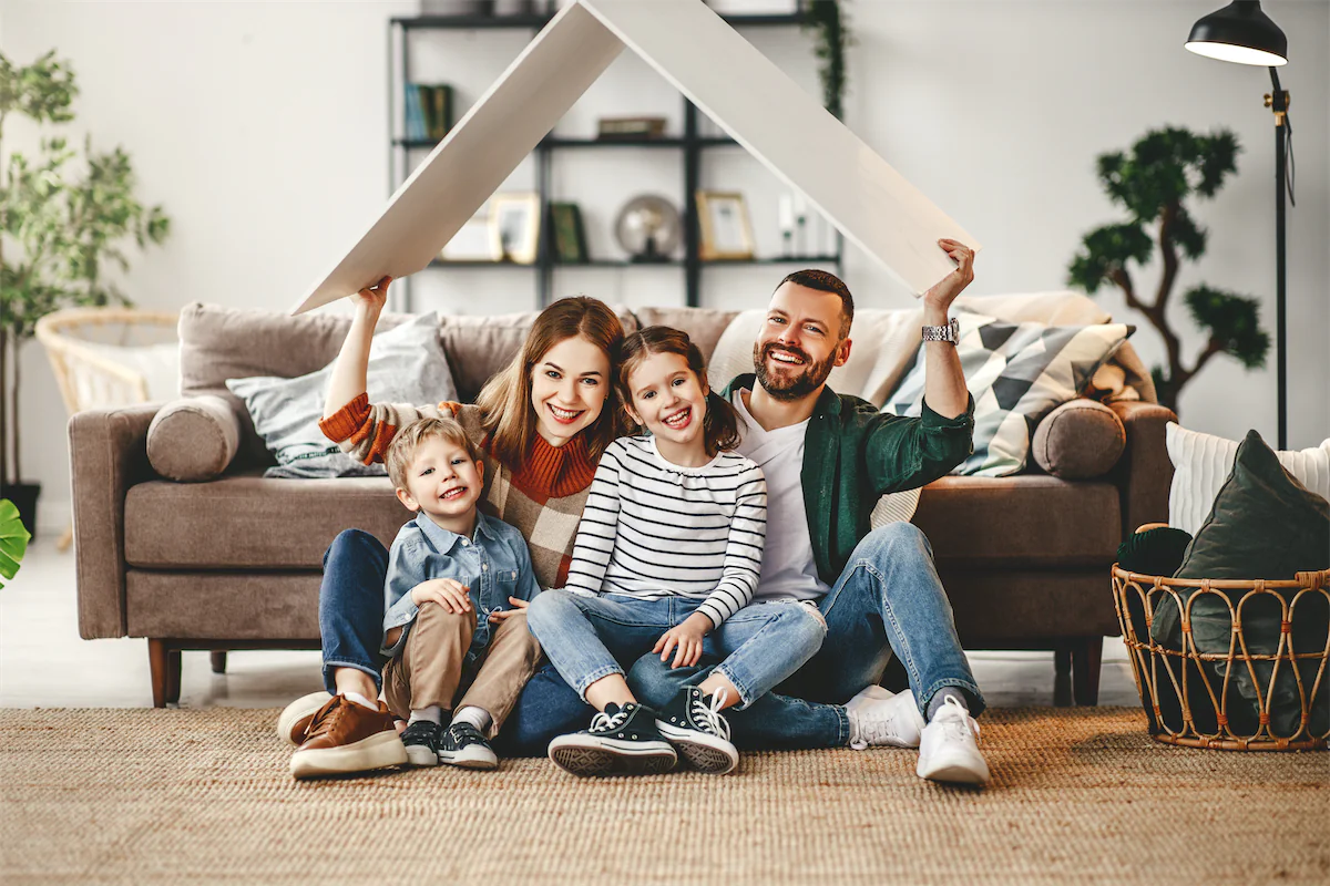 Smiling family of four holding a small triangular roof over their heads